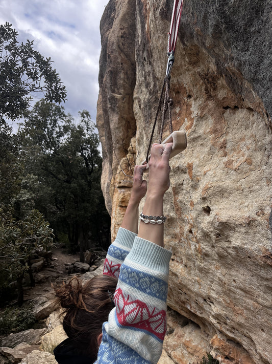 Close-up of a climber gripping a FIKA Pinnbröd wooden board by a lead climbing crag.