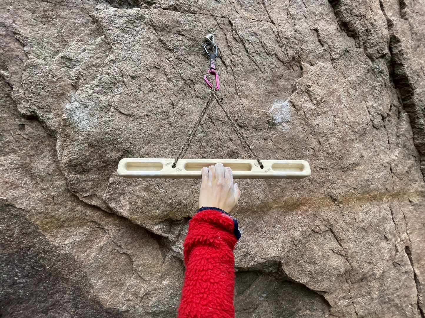 Climber using the FIKA Pinnbröd wooden hangboard on a granite cliff face.