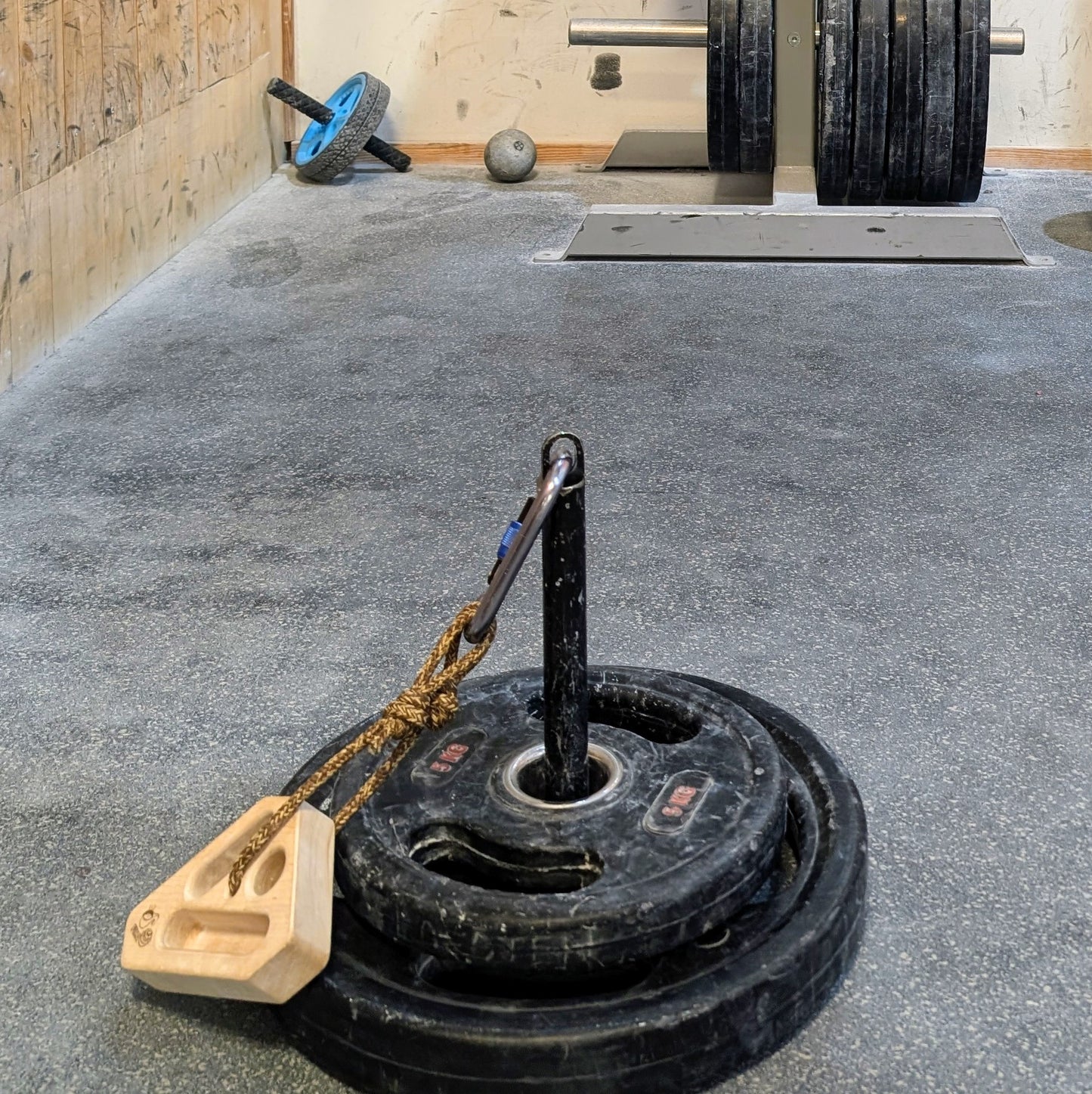 FIKA Rullrån steel loading pin with weights attached to a wooden grip block.