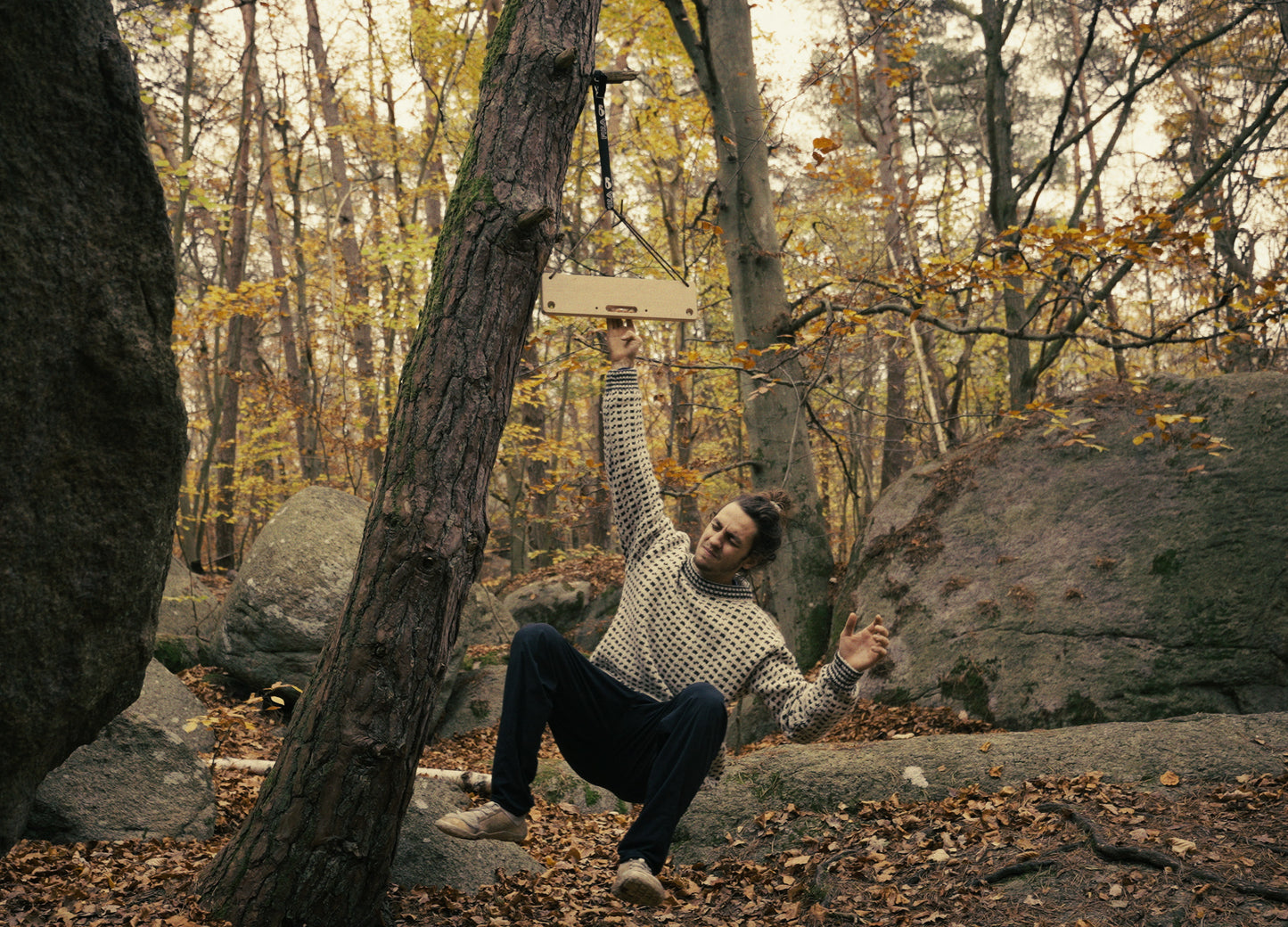 Climber performing a one-arm hang on the portable Vetelängd wooden board in an autumn forest.
